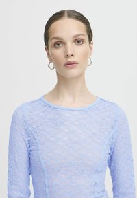 Top in pizzo azzurro chiaro con maniche lunghe e scollo rotondo, caratterizzato da un motivo floreale e una texture morbida e trasparente.