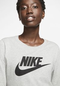 Felpa grigia con un prominente logo Nike nero. Il materiale sembra morbido, con un design classico a girocollo e tessuto testurizzato.