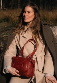 Red leather handbag with soft texture, rounded shape, and dual handles. Features a flap closure and subtle stitching details.