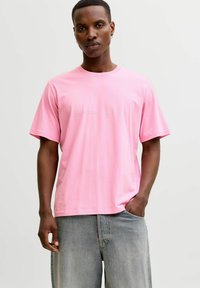 Camiseta rosa de algodón con mangas cortas, con texto blanco de marca en el frente, combinada con shorts de mezclilla azul claro. Diseño sencillo y ajuste relajado.