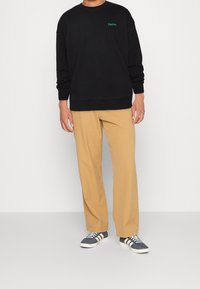 Černá bavlněná mikina s zelenou výšivkou, béžové kalhoty a námořnické tenisky s bílými pruhy. Volný střih, žebrované manžety a lem.