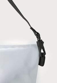 Gjennomsiktig vanntett bag med en glatt tekstur, svart justerbar stropp og plastspenne, med et minimalistisk design.