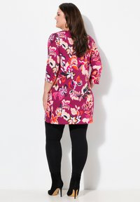 Abito tunica floreale nei toni di viola, rosa e arancione con maniche tre quarti, abbinato a leggings neri e stivali neri con tacco alto.