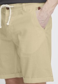 Shorts beiges en tissu léger, dotés d'un cordon de serrage en corde, de poches latérales et d'un ourlet replié pour un look décontracté.