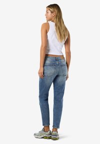 Hvit ribbet crop-topp, falmede blå jeans med lys vask, og grå joggesko med grønne detaljer. Synlige detaljer på baklommen på jeansen.