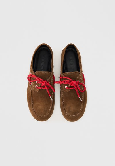 Smeđe nubuk cipele s crvenim vezicama, sa zaobljenim vrhom, kontrastnim šavovima i teksturiranom potplatom. Jednostavan dizajn s minimalnim akcentima.