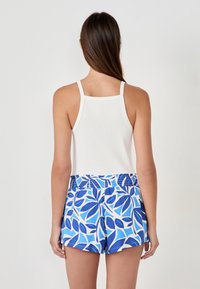 Débardeur blanc à rayures associé à un short bleu à motifs avec un design de feuilles. Le short a une taille élastique et des poches latérales.