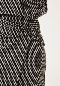 Tela con un estampado negro y crema que cae con un detalle anudado en la cintura. El diseño geométrico presenta formas de diamante y una textura suave.