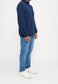 Marinblå polotröja med ribbade muddar, matchad med ljusblå jeans och vita sneakers med grå detaljer.