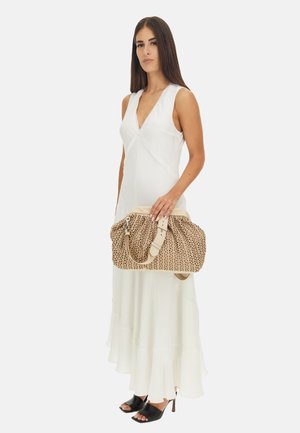 Borsa marrone a motivo con una superficie strutturata, manici crema e accessori in argento, tenuta da una persona in un abito bianco. Scarpe nere con le dita dei piedi scoperte visibili.