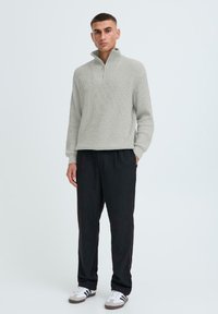 Helles graues geripptes Pullover mit einem Viertelreißverschluss, kombiniert mit schwarzen Hosen und weißen Sneakern mit schwarzen Streifen an den Seiten.