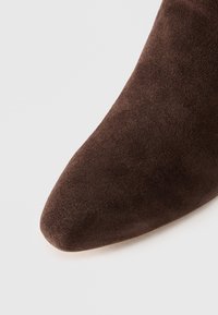 Brune suède ankelstøvler med spiss tå-design. Teksturen er myk, med en matt finish uten synlig maskinvare eller mønstre.