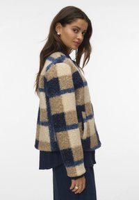 Geruite jas met fleece materiaal in beige en marineblauw. Licht oversized model met open voorkant, zijzakken en een afgeronde kraag.