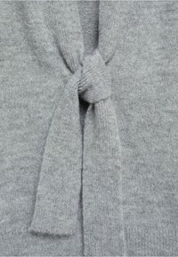 Tissu gris doux tricoté, noué en un simple nœud, montrant en gros plan la texture et les détails des points.