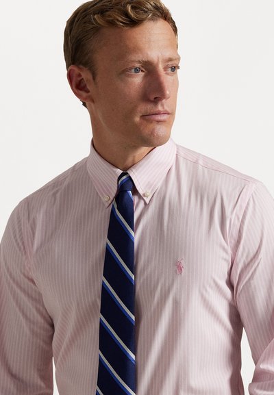 Camisa de vestir de rayas rosa claro con cuello abotonado, que cuenta con un pequeño logotipo bordado en el pecho, combinado con una corbata de rayas azules.