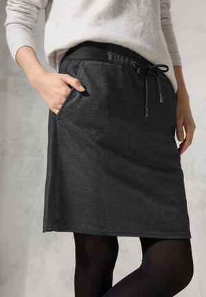 Zwarte gebreide rok met een trekkoord in de taille, voorzien van zijzakken en een textuurstof. Draag met zwarte maillot.