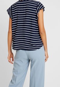 Top a righe blu navy con maniche corte, caratterizzato da un collo rotondo e un orlo leggermente curvo. Abbinato a pantaloni larghi azzurri.