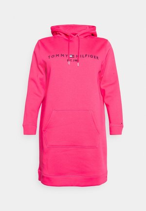 Jasnoróżowa długa sukienka z kapturem, z kieszenią z przodu, kapturem ze sznurkiem oraz napisem i logo "Tommy Hilfiger Est. 1985" na piersi.