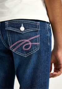 Mørkeblå denimjeans med et lyserødt broderet mønster på baglommen, en sølvknap og traditionelle lommedetaljer.