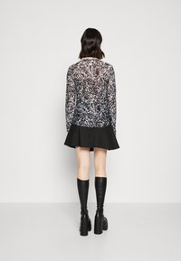 Langärmlige Bluse mit schwarz-weißem Muster und transparenter Textur, kombiniert mit einem schwarzen, ausgestellten Rock und kniehohen schwarzen Stiefeln mit Absatz.