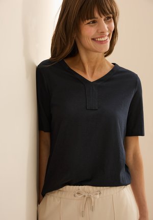 Marineblauwe korte mouwen shirt met een V-hals en horizontale naaddetails, gecombineerd met beige broeken met trekkoord. Zacht materiaal en een relaxte fit.