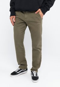 Pantalons en mélange de coton olive avec une coupe slim, poches avant et détails de couture, associés à des baskets noires à tige basse.