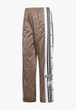 Pantalones deportivos marrones con estampado de jirafa, paneles laterales blancos con rayas negras de Adidas y botones de presión a lo largo de la pierna.