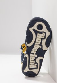 Timberland plava sandala s žutim akcentima, koja ima teksturiranu gumenu potplat, podesivu traku i istaknuti logo na dnu.
