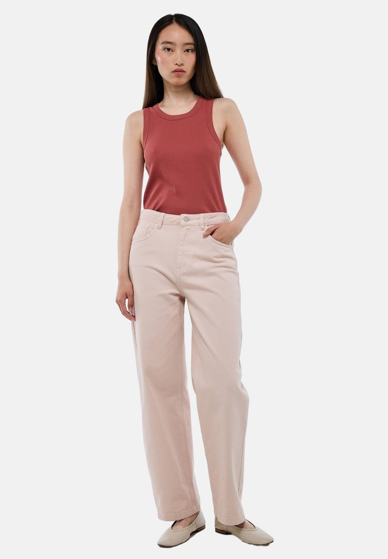 Pantalons taille haute rose clair avec une coupe droite, associés à un débardeur ajusté de couleur rouille. Des chaussures plates complètent la tenue.