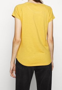 Żółta koszulka z krótkim rękawem, z zaokrąglonym dołem i rękawami raglanowymi. Wykonana z lekkiego materiału o miękkiej fakturze.