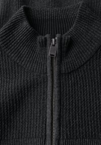 Mörkgrå ribbad stickad tröja med hög krage och en centralt placerad metalldragkedja där det står "STREET ONE MEN" ingraverat på dragfliken.