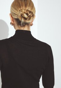 Suéter negro de cuello alto que muestra un diseño ajustado con una textura acanalada y un cuello alto, estilizado con un peinado de moño bajo y pendientes sencillos.