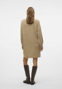 Abito beige a maglia con maniche a treccia, lunghezza al mid-thigh e vestibilità morbida, abbinato a stivali marroni scuri al ginocchio.