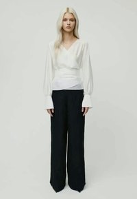 Blusa branca envolvente com mangas longas, combinada com calças largas de riscas pretas, apresentando um ajuste descontraído e detalhes de textura subtil.