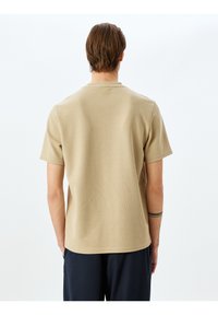 Beige T-Shirt mit kurzen Ärmeln aus strukturiertem Stoff, rundem Halsausschnitt, geradem Saum und schlichtem Design.