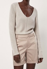 Strickpullover in hellem Beige mit tiefem V-Ausschnitt und geripptem Design, kombiniert mit hellbeigen, maßgeschneiderten Shorts mit umgeschlagenen Säumen und seitlichen Taschen.