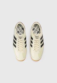 Crèmekleurige sneakers met drie zwarte strepen, een gestructureerd leren bovenwerk en een gumrubberen zool. Voorzien van een logo op de tong en een patroon op de binnenzool.