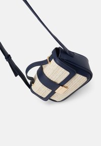 Borsa a mano blu navy con pannello intrecciato beige, forma rettangolare, dettagli in hardware dorato e tracolla regolabile. Superficie con texture.
