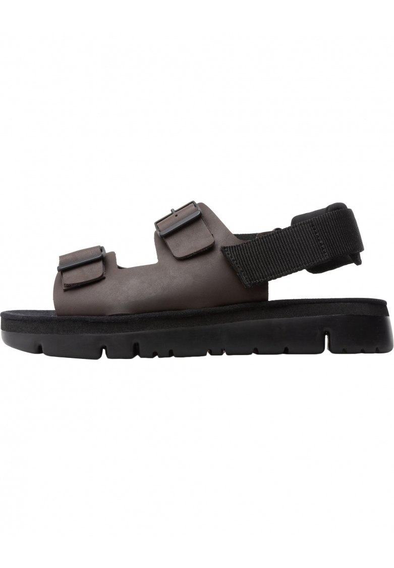 Brown sandals made of synthetic material with a textured strap, two adjustable metal buckles, and a thick black rubber sole.