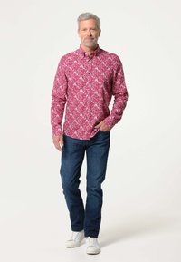 Rode bloemen lange mouw shirt met een button-down kraag, gecombineerd met blauwe jeans en witte sneakers. De stof heeft een gladde textuur.
