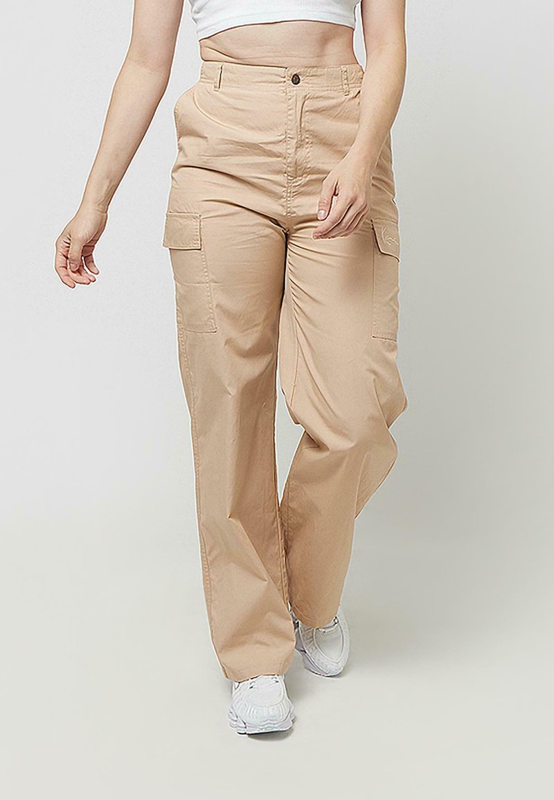 Bež hlače cargo iz lahkega blaga s sproščenim krojem, z bočnimi žepi in visokim pasom. Kombinirane z belimi supergami.