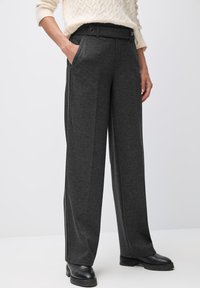 Pantalons larges gris en tissu doux, dotés d'une ceinture avec boutons et de poches latérales, complétés par de subtils accents rayés.