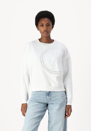 Felpa bianca con dettaglio logo circolare in rilievo, collo a giro, maniche lunghe, abbinata a jeans in denim azzurro chiaro.