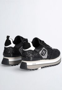 Svarta sneakers med en strukturerad ovandel med glittrande detaljer, vita och grå designinslag samt en tjock sula med grepp.