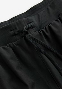 Shorts de sport noirs avec une texture lisse, dotés d'une taille élastique avec un cordon de serrage pour un ajustement et un design minimaliste.