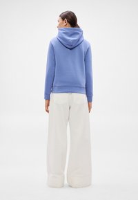 Sudadera con capucha de color azul claro, textura suave y mangas largas, combinada con pantalones blancos de cintura alta y pernera ancha con bolsillos traseros visibles.