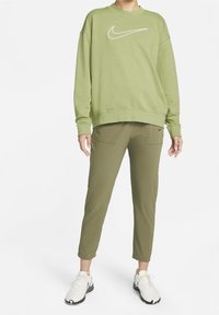 Sweatshirt en coton vert avec logo Nike blanc, associé à un pantalon de jogging olive avec poches latérales et des chaussures de sport blanches.