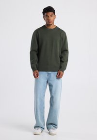 Dark green sweater with a crew neckline, long sleeves, and ribbed cuffs, paired with light blue wide-leg jeans and white sneakers.
