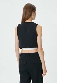 Schwarzes, kurzes Oberteil mit strukturiertem Design, ärmellosem Stil und glatter Textur, kombiniert mit hochsitzzenden dunklen Hosen.
