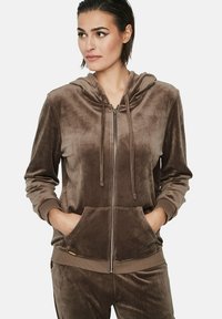 Hoodie zippé en velours marron avec capuche à cordon, poches avant et poignets côtelés. Texture douce et finition lisse.
